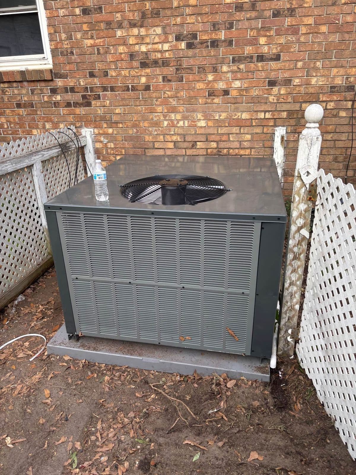 Condenser beside a brick wall and lattice fence