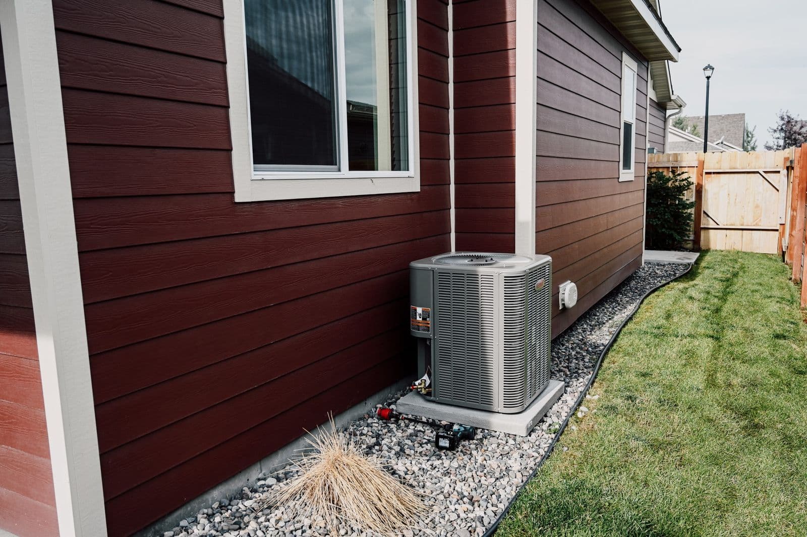 Newly installed condenser beside a house with dark red siding