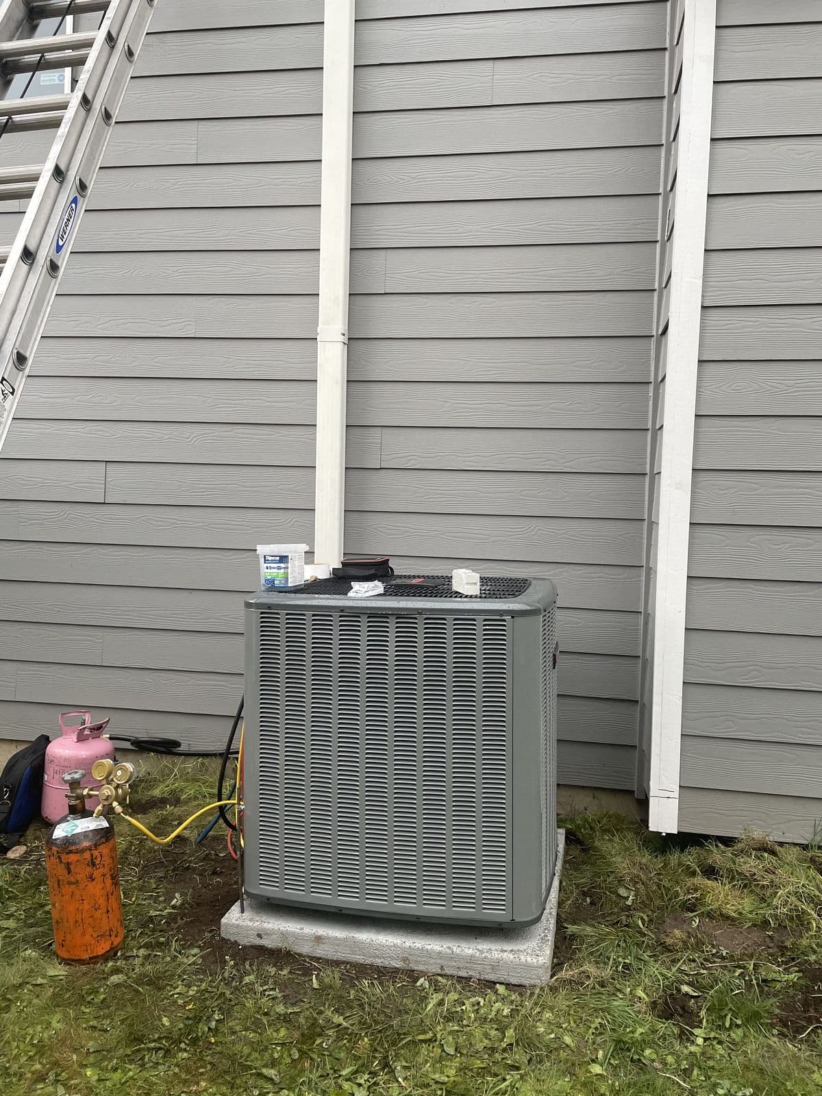 Condenser on a pad beside a gray house with a refrigerant tank