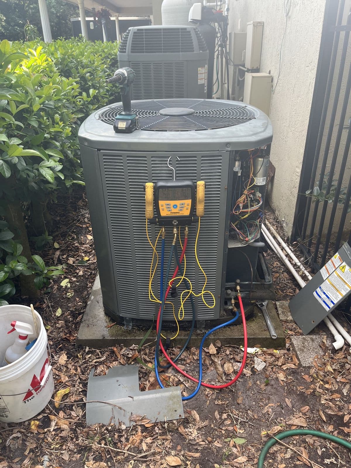 Outdoor air conditioner with gauges attached during a repair beside a house