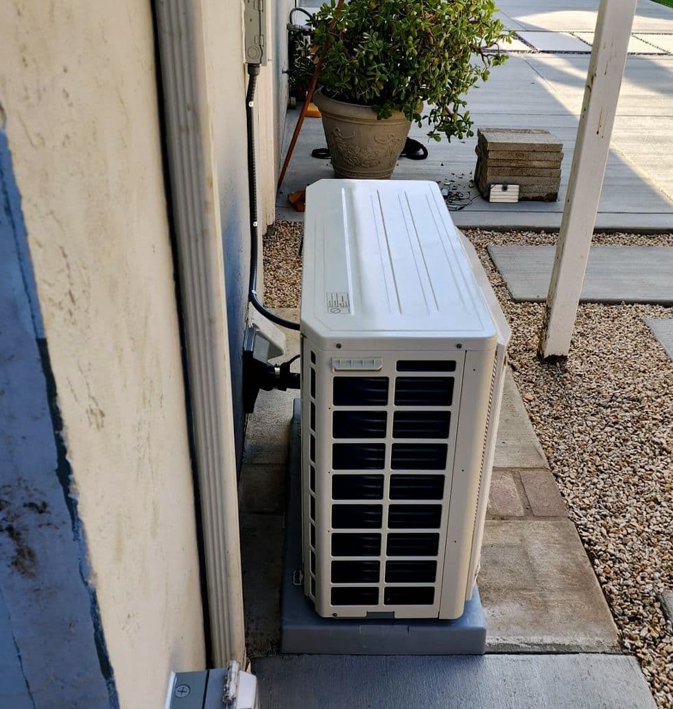 Mini split outdoor unit tucked beside a house on pavers