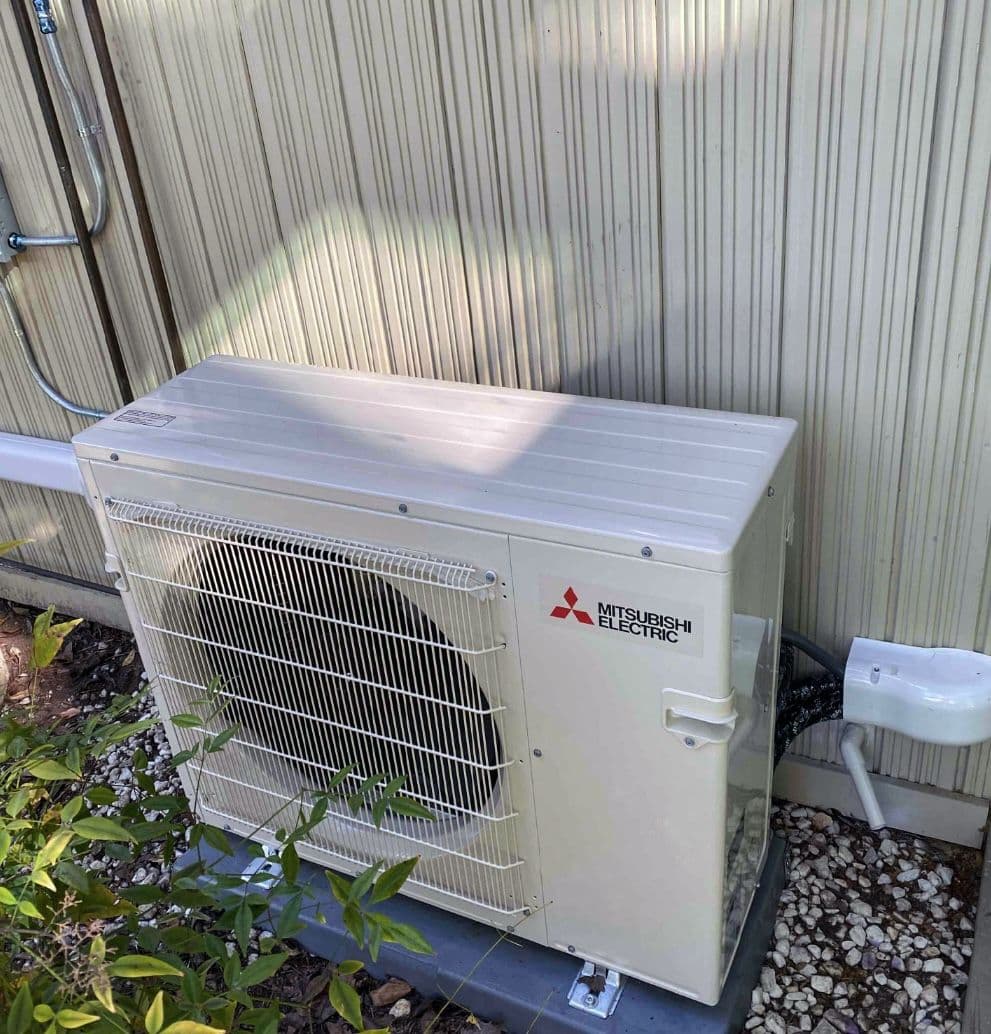 Mitsubishi mini split outdoor unit on a pad beside siding