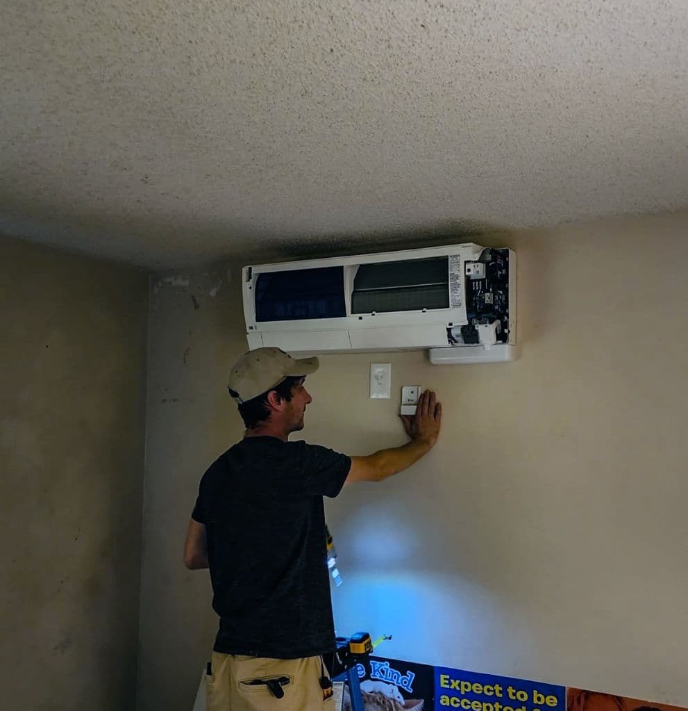 Technician installing a ductless wall unit in a small room