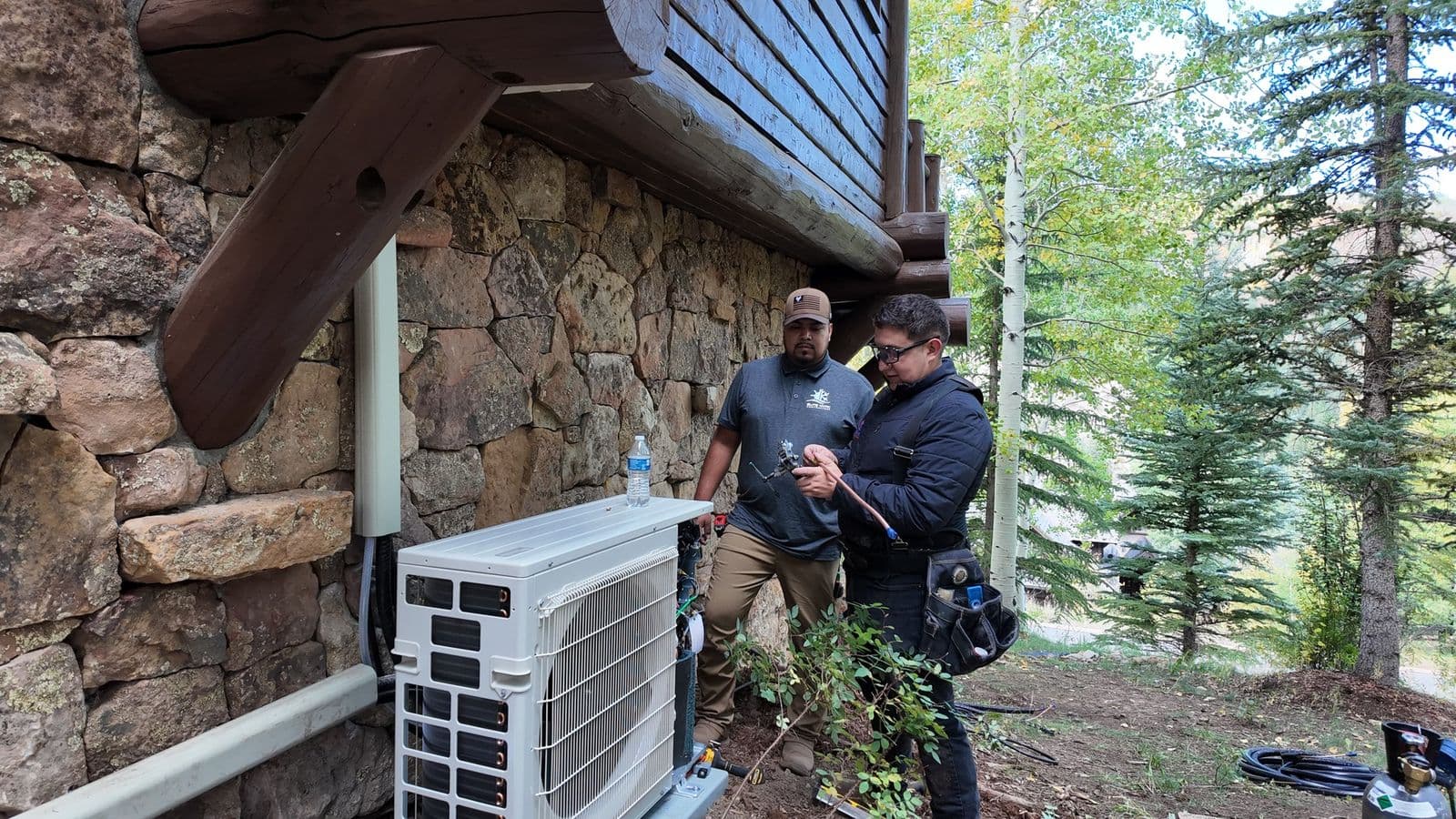 Two technicians installing a mini split outside a stone house