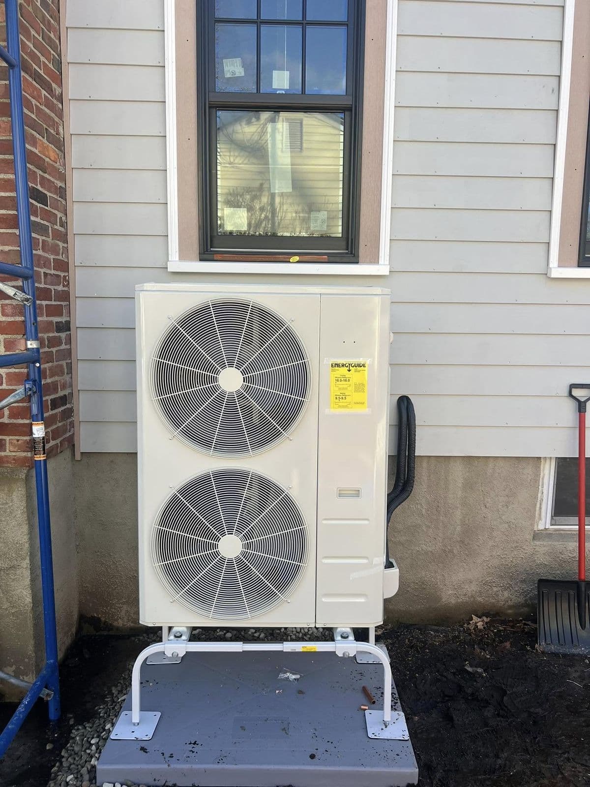 Dual fan heat pump mounted on a stand beside a house