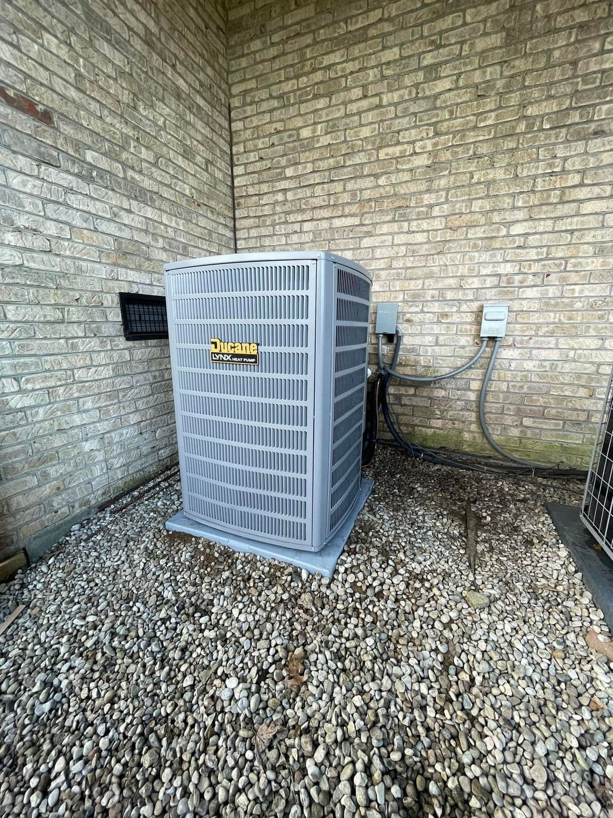 Heat pump on a gravel bed beside a brick wall