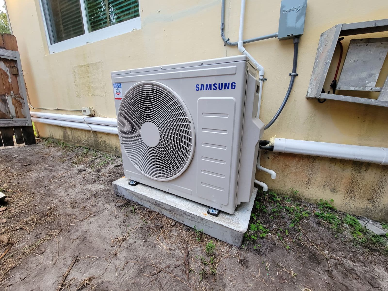 Mini split heat pump outdoor unit on a pad beside a stucco house