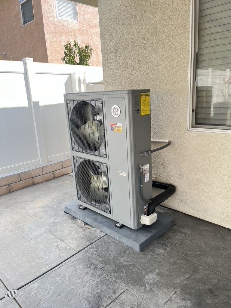 New dual fan heat pump on a pad beside a house