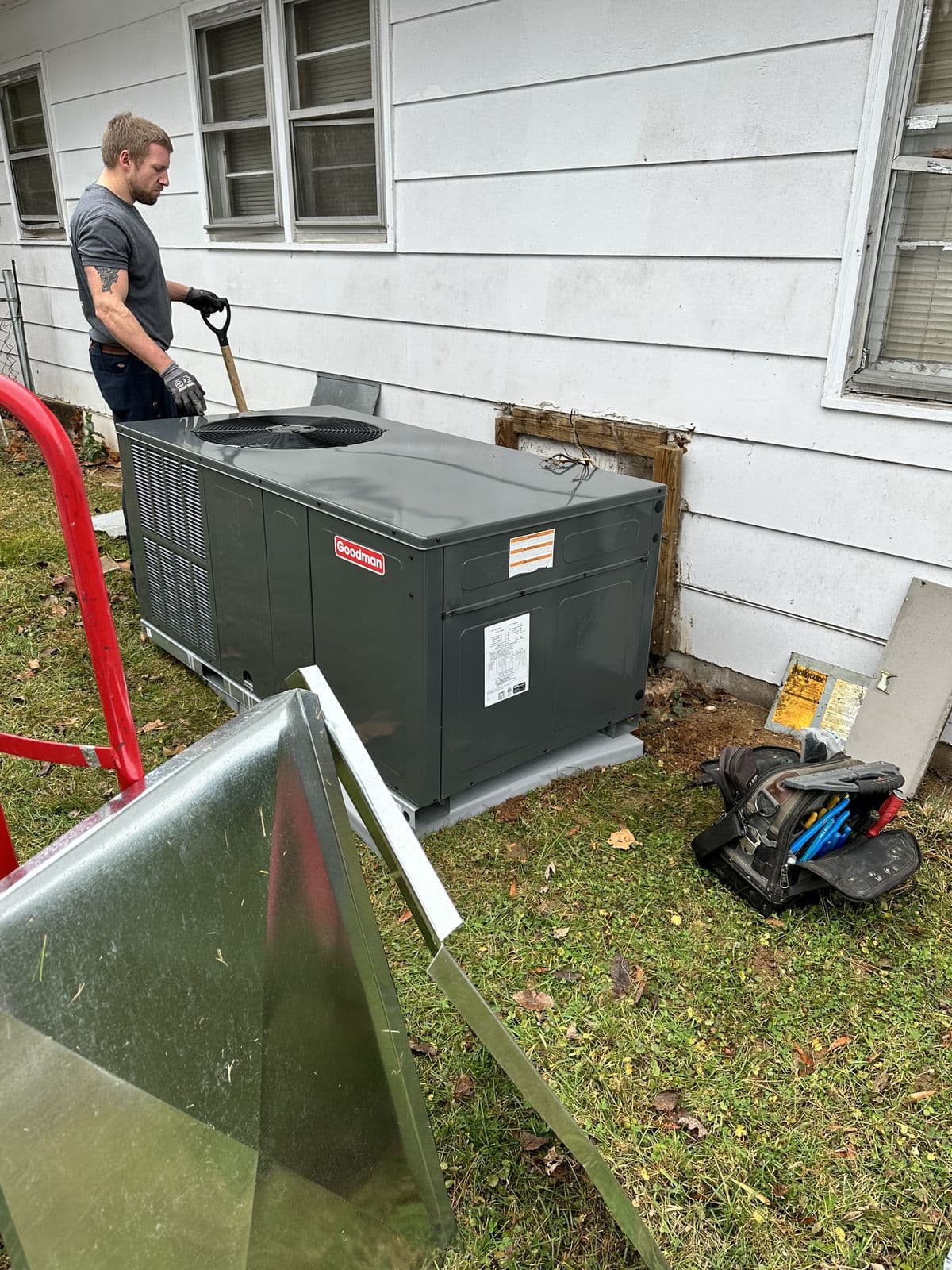 Technician cleaning a packaged unit beside a house