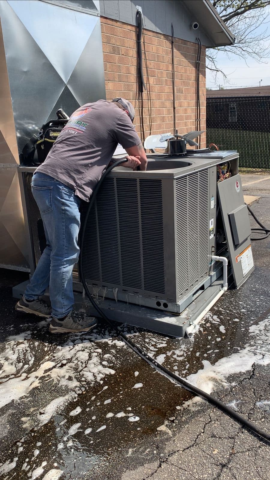 Technician cleaning an outdoor air conditioner with water
