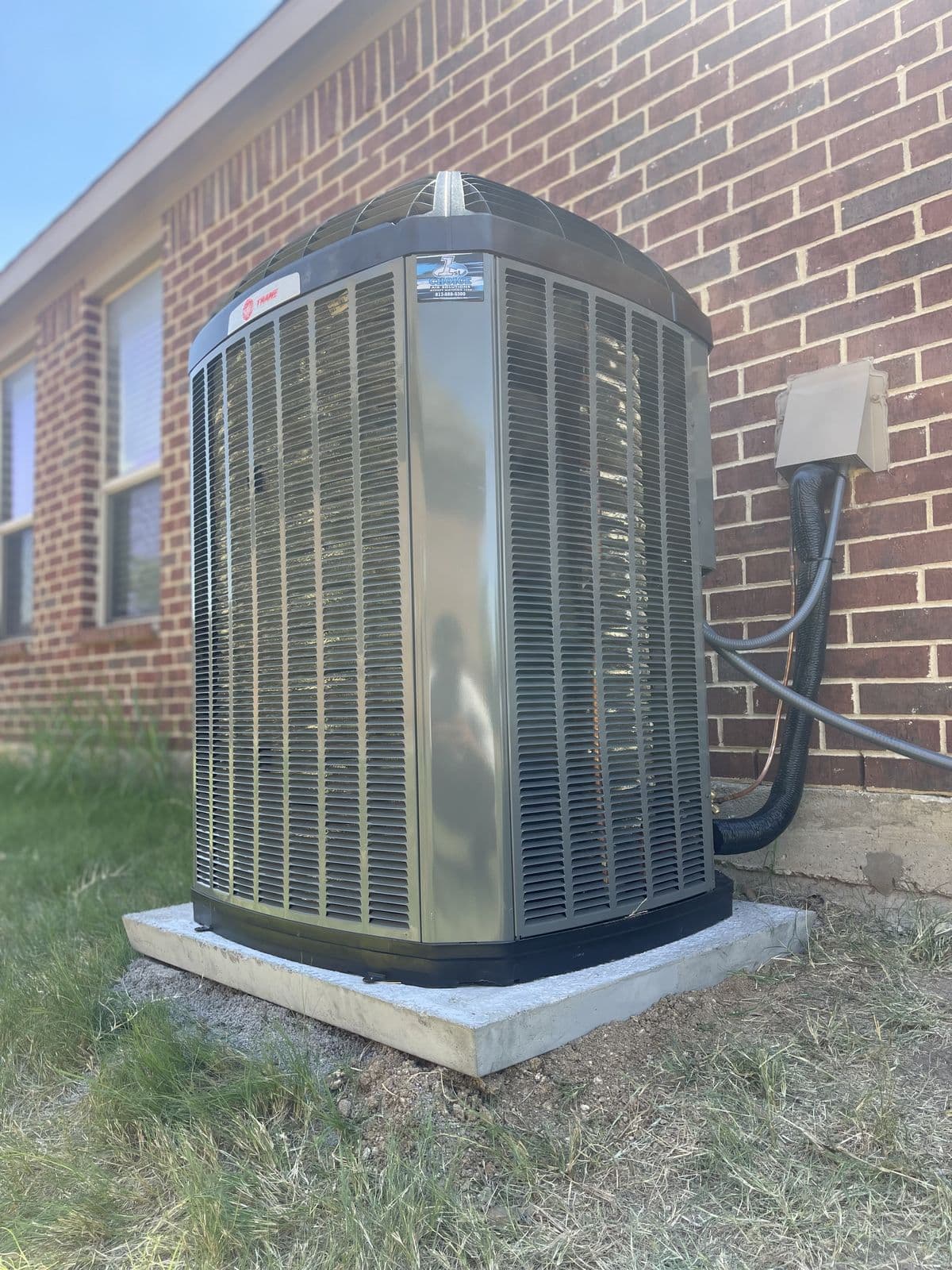 Condenser on a concrete pad beside a brick wall