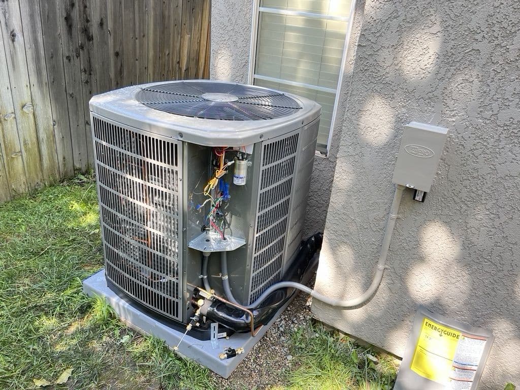 Outdoor unit with the access panel open on a concrete pad beside a stucco wall