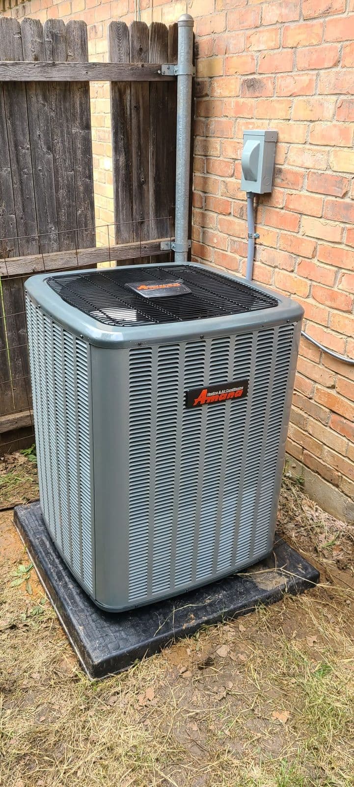 New outdoor air conditioner on a pad beside a brick wall and wood fence
