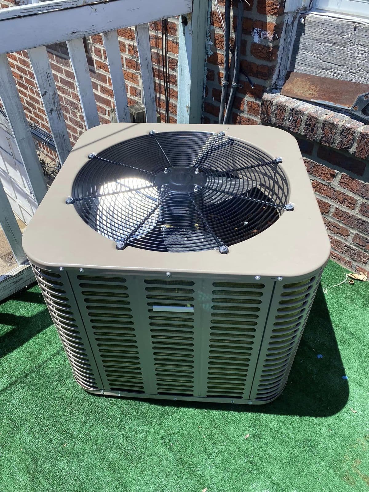 New outdoor unit on a green turf pad beside a brick wall