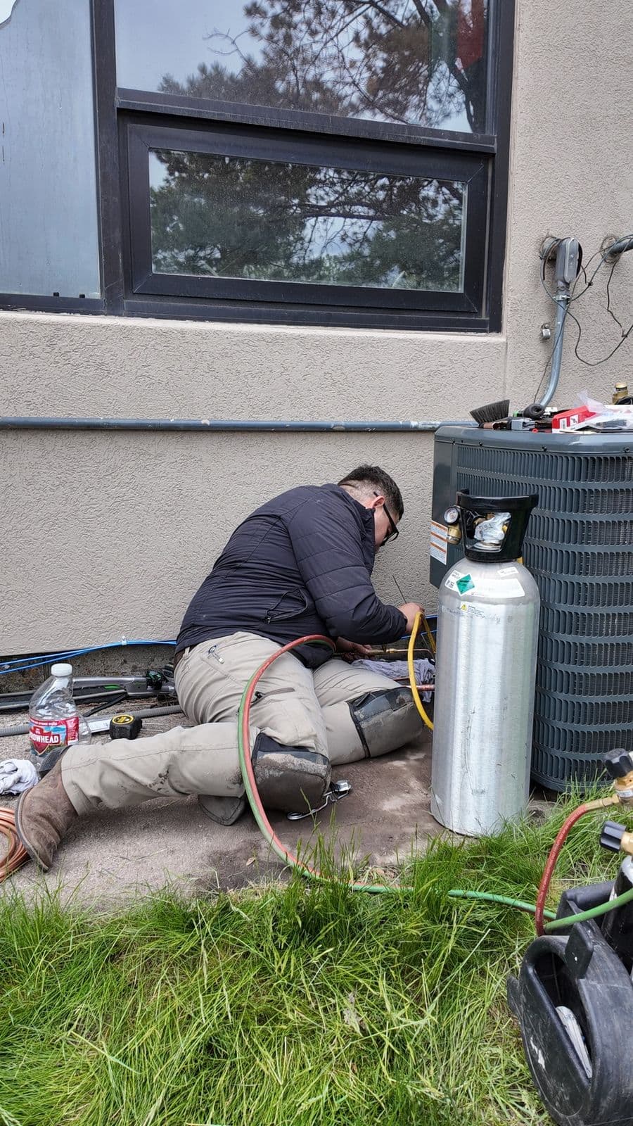 Technician with gauges and a refrigerant tank servicing an air conditioner