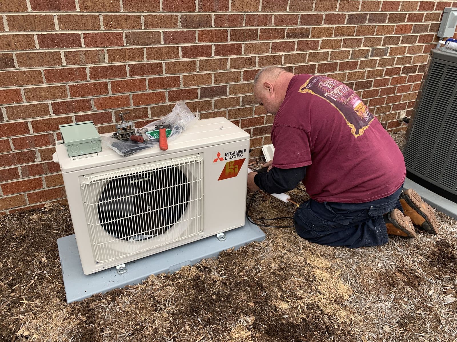 Technician installing a mini split outdoor unit on a pad