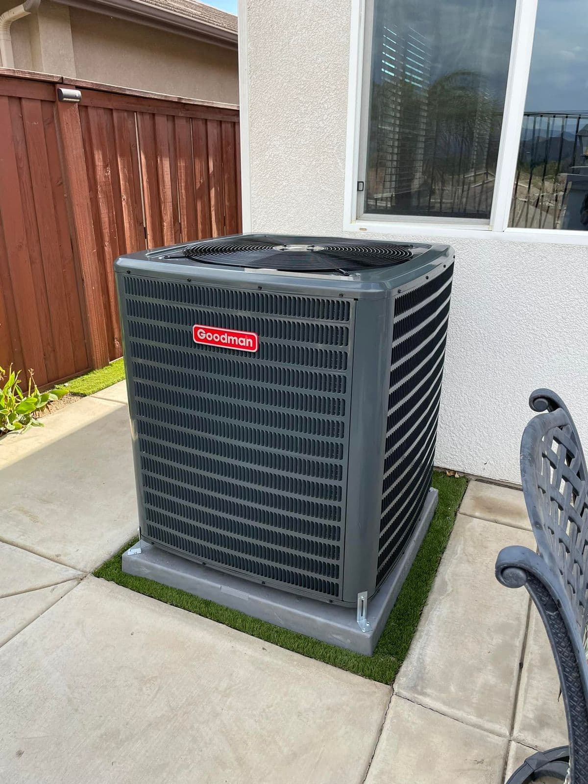 Outdoor unit on a turf pad beside a stucco wall