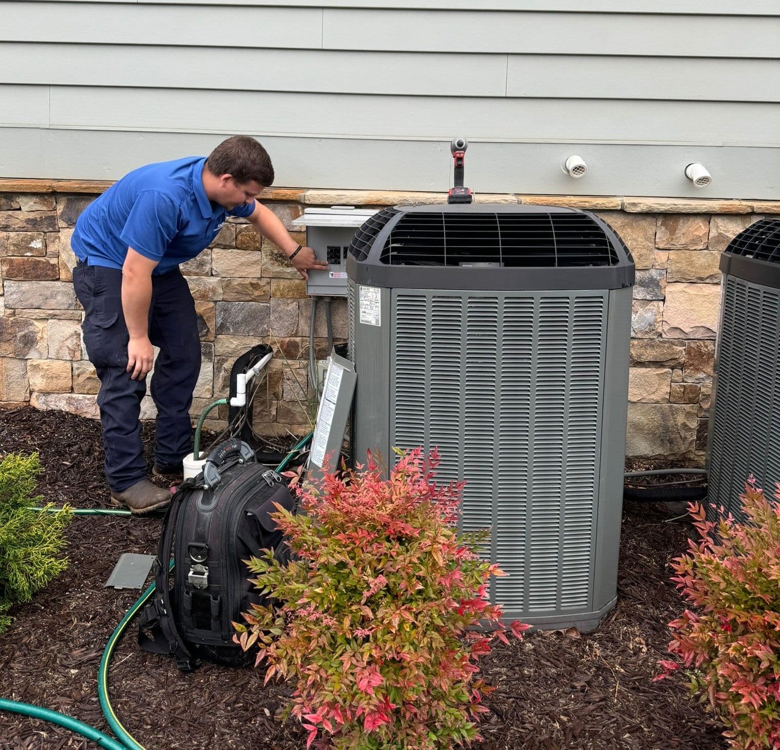 Technician rinsing an outdoor unit's coil with a garden hose during a tune up